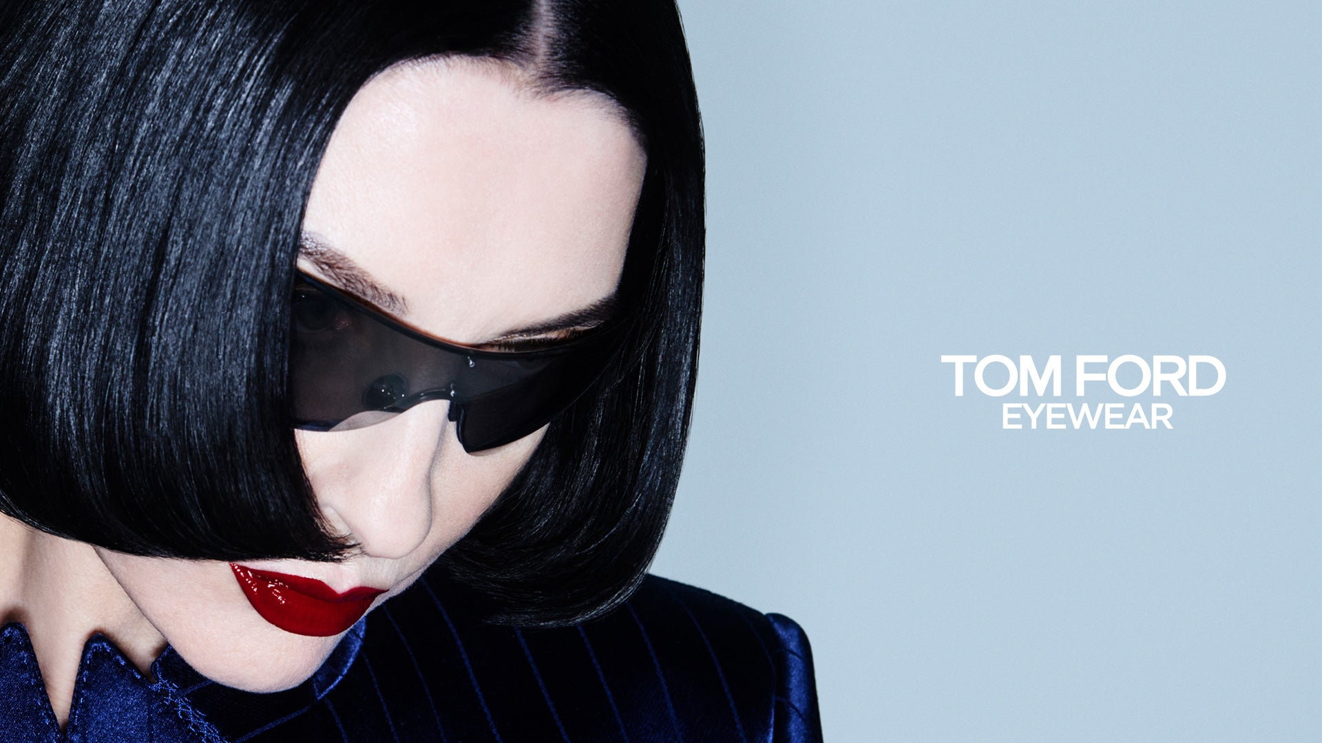 Person wearing a black eye mask with 'Tom Ford Eyewear' branding on a gray background